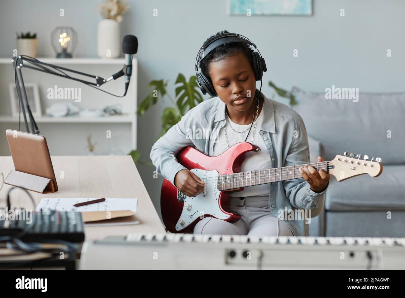Retrato de una joven mujer negra tocando guitarra eléctrica y grabando canciones en estudio en casa, espacio de copia Foto de stock