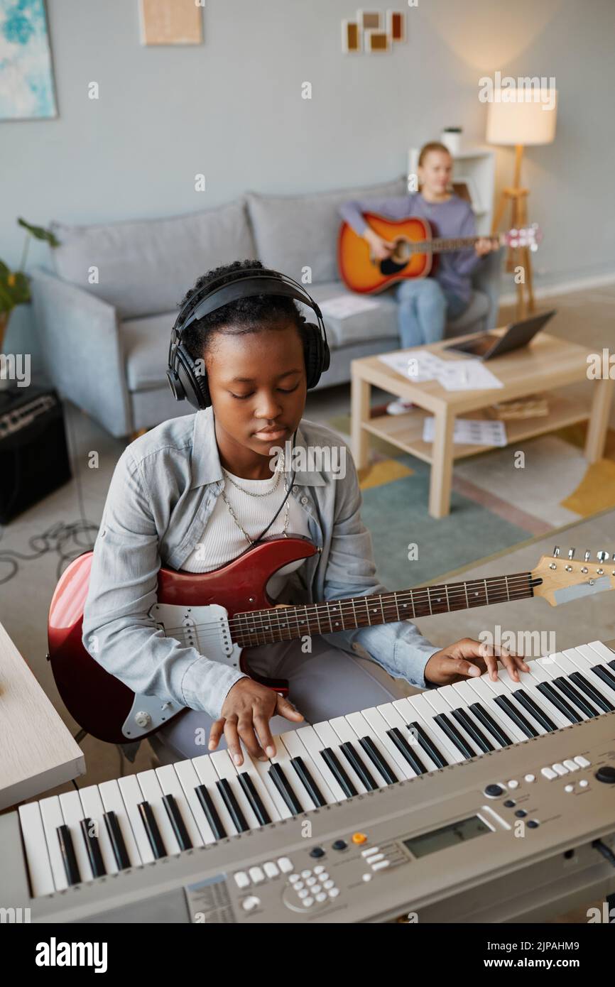 Retrato vertical de una joven negra que toca música en casa y lleva auriculares Foto de stock