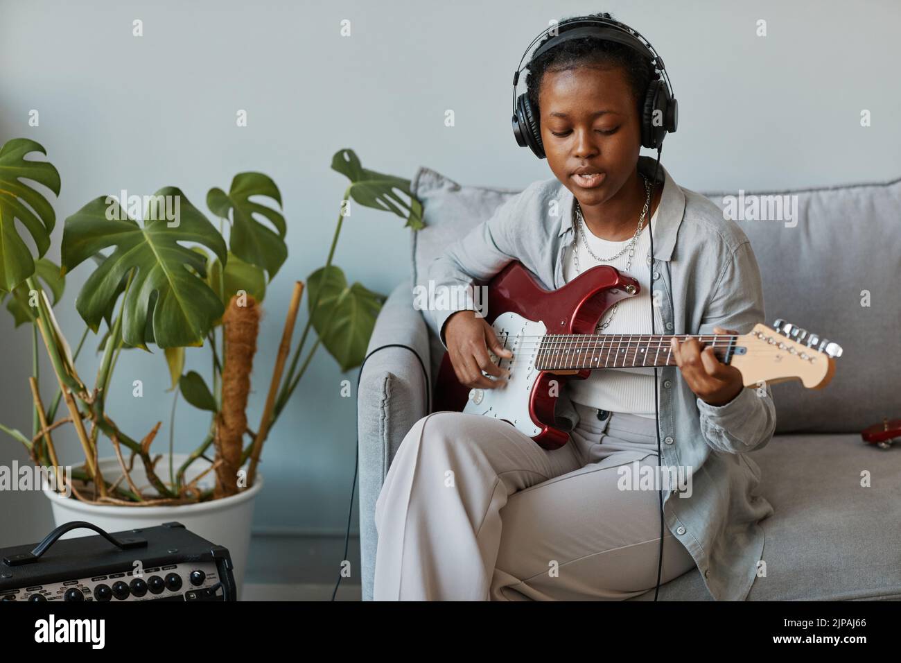 Retrato mínimo de una joven negra tocando la guitarra electrónica en casa y cantando, espacio de copia Foto de stock