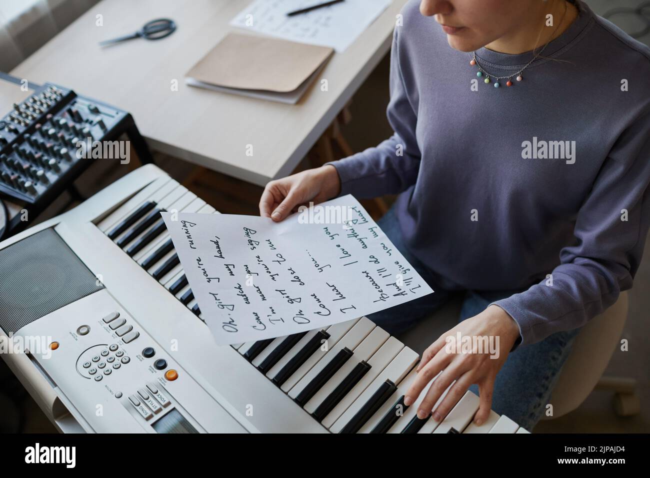 Primer plano de un joven músico tocando el sintetizador en casa y sosteniendo la hoja de letras de canciones, espacio de copia Foto de stock