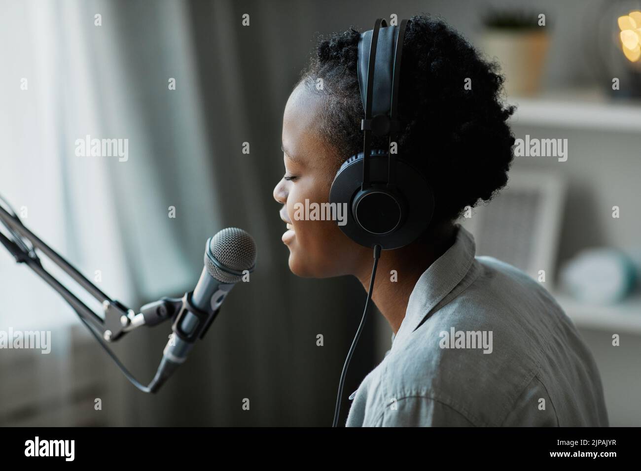 Vista lateral mínima de la joven músico que canta al micrófono en casa y lleva auriculares, espacio para copias Foto de stock