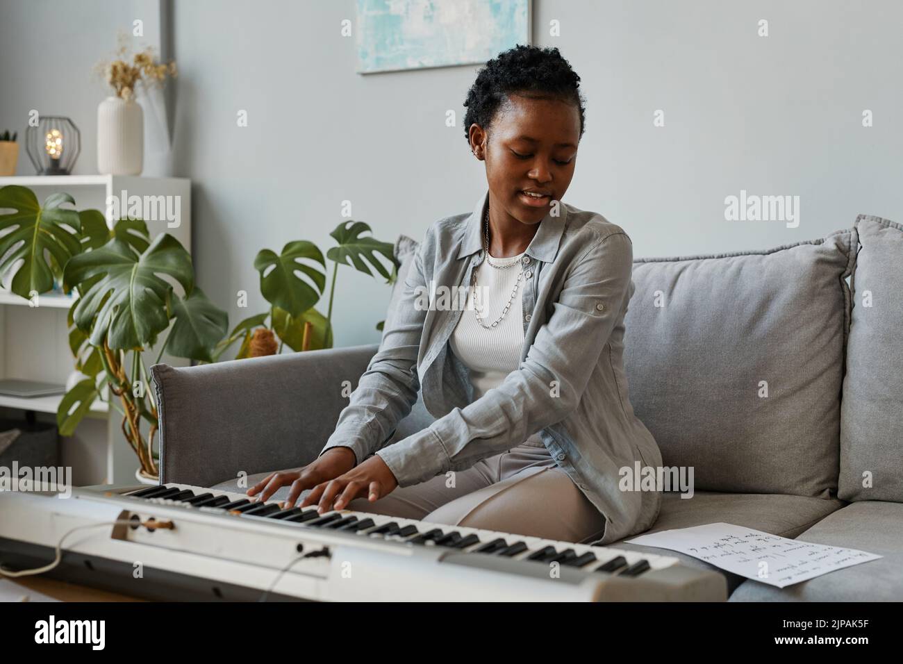 Retrato de una joven mujer negra tocando el sintetizador en casa y componiendo música en un ambiente acogedor, espacio de copia Foto de stock
