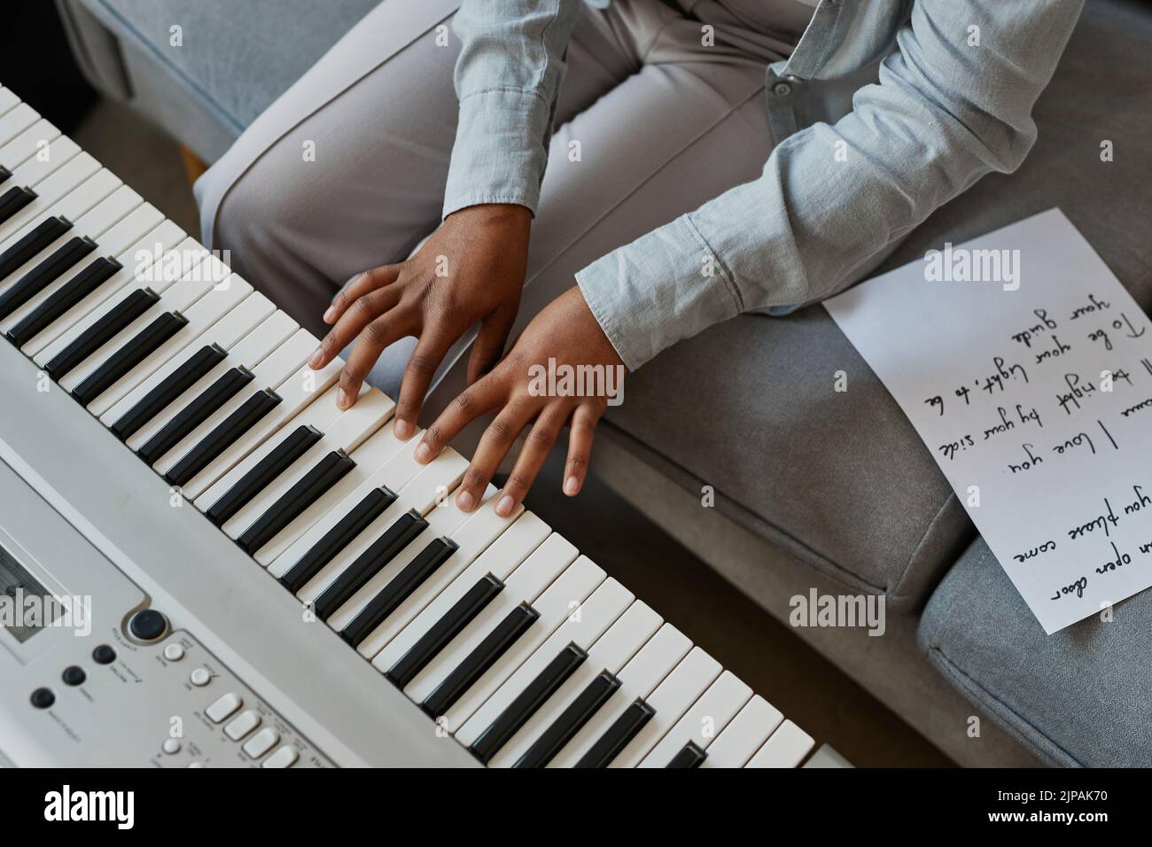 Vista superior Primer plano de la joven mujer pulsando las teclas de piano mientras compone música en casa con letras de canciones, espacio de copia Foto de stock