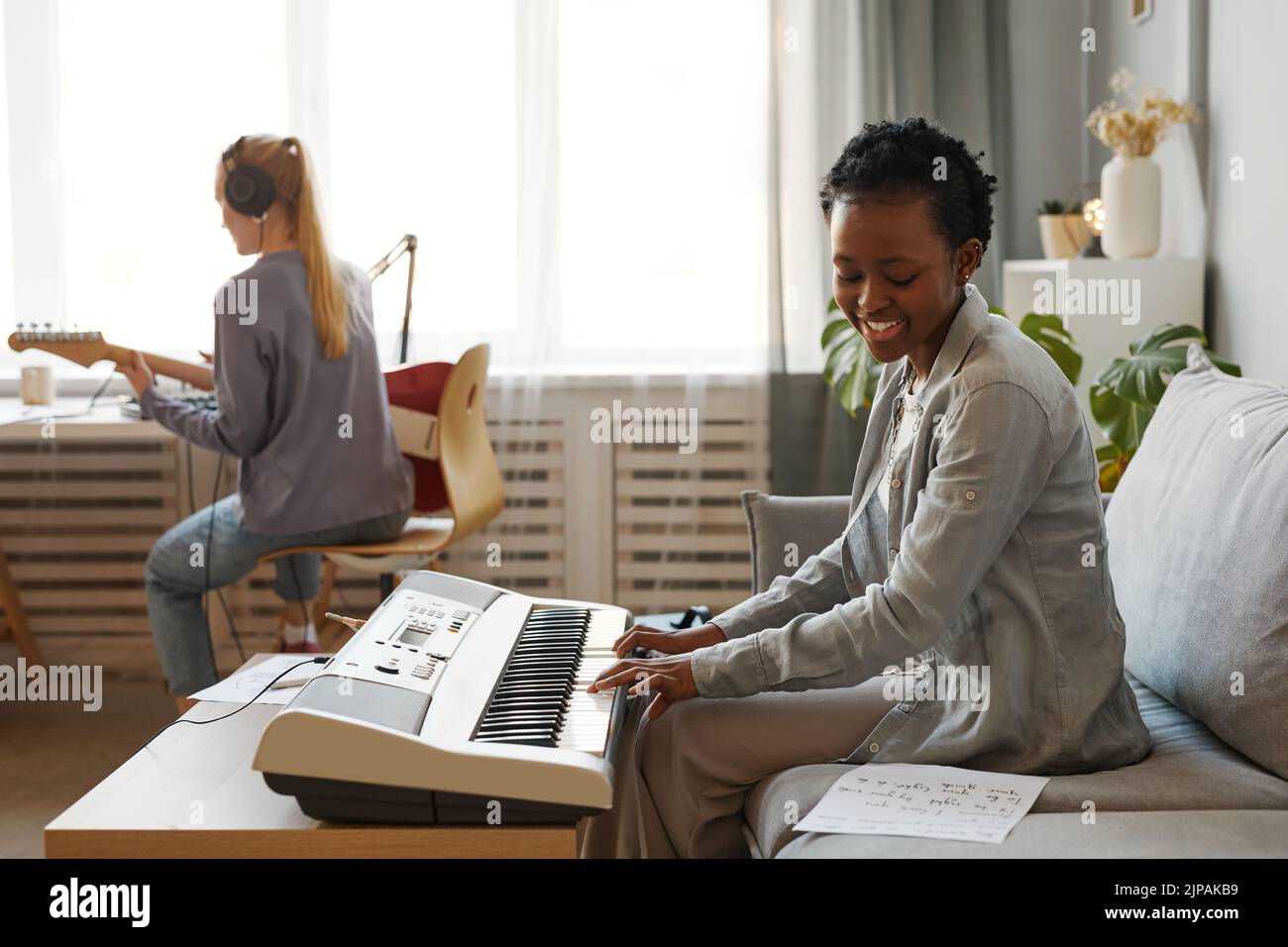 Vista lateral retrato de sonriente mujer negra tocando sintetizador en casa y componiendo música en el estudio, espacio de copia Foto de stock