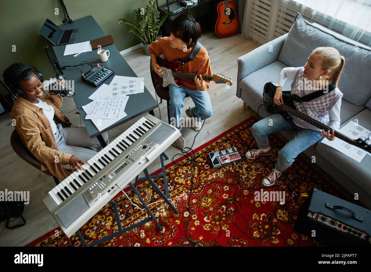 Vista superior de la banda de jóvenes músicos tocando instrumentos juntos en un acogedor estudio en casa Foto de stock