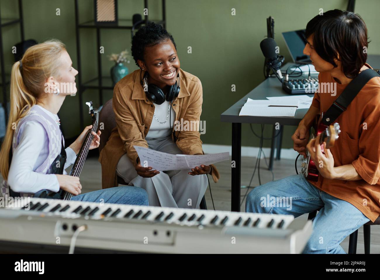 Retrato de tres jóvenes músicos escribiendo canciones juntos, se centran en una mujer negra sonriendo felizmente y sosteniendo una hoja de música Foto de stock