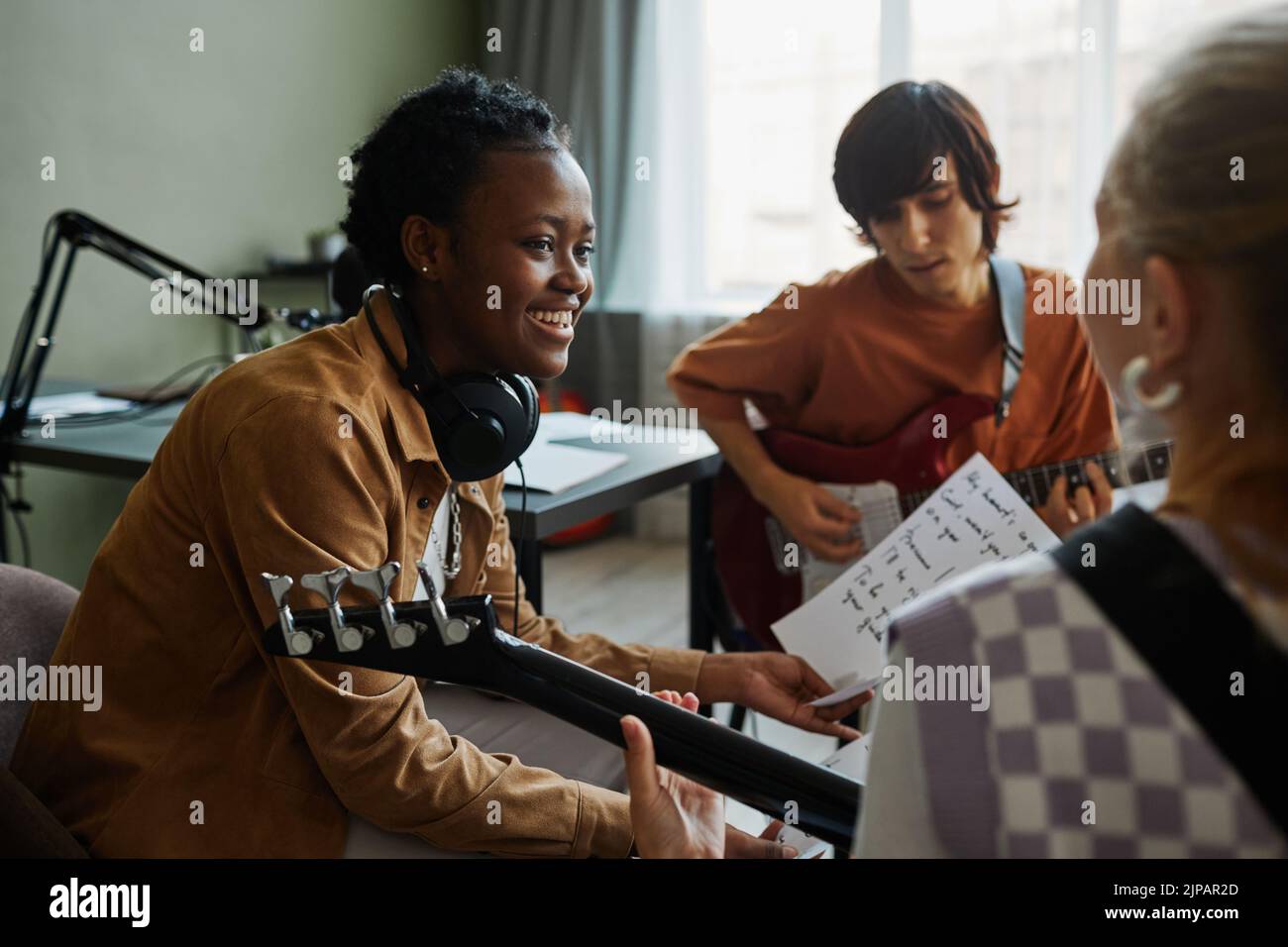 Vista lateral retrato de mujer joven negra escribiendo música con banda y sonriendo felizmente Foto de stock