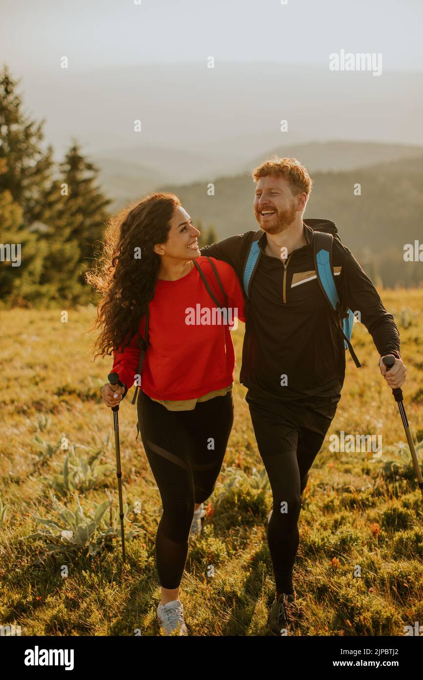 Una pareja joven sonriente caminando con mochilas sobre verdes colinas Foto de stock