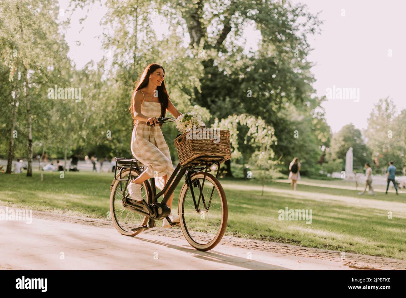 Una mujer joven y bonita con bicicleta eléctrica y flores en la cesta Foto de stock