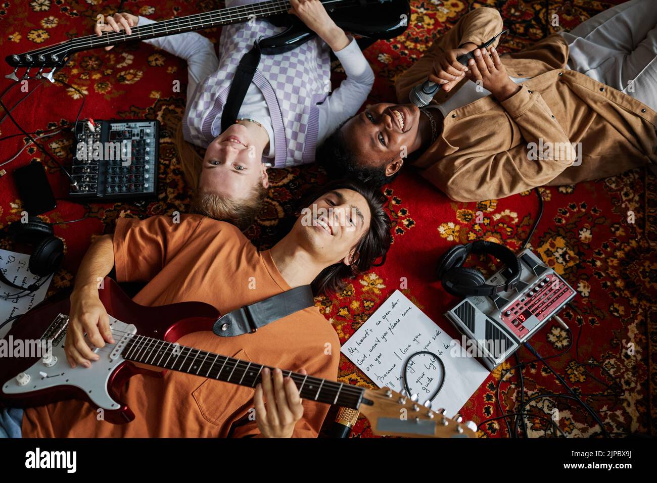 Imagen superior de una sonriente banda musical tumbada en una alfombra ornamentada en un estudio de mucis mirando a la cámara Foto de stock