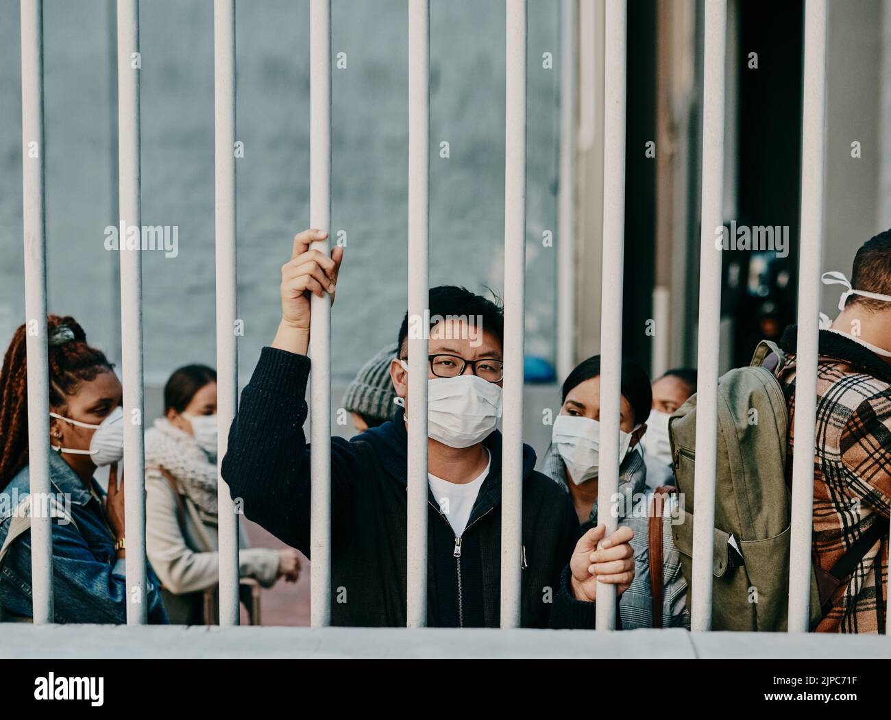Detrás de las rejas, el cierre y covid restricciones con un hombre usando una máscara durante una pandemia y prohibición de viajar. Retrato de un hombre bloqueado durante Foto de stock