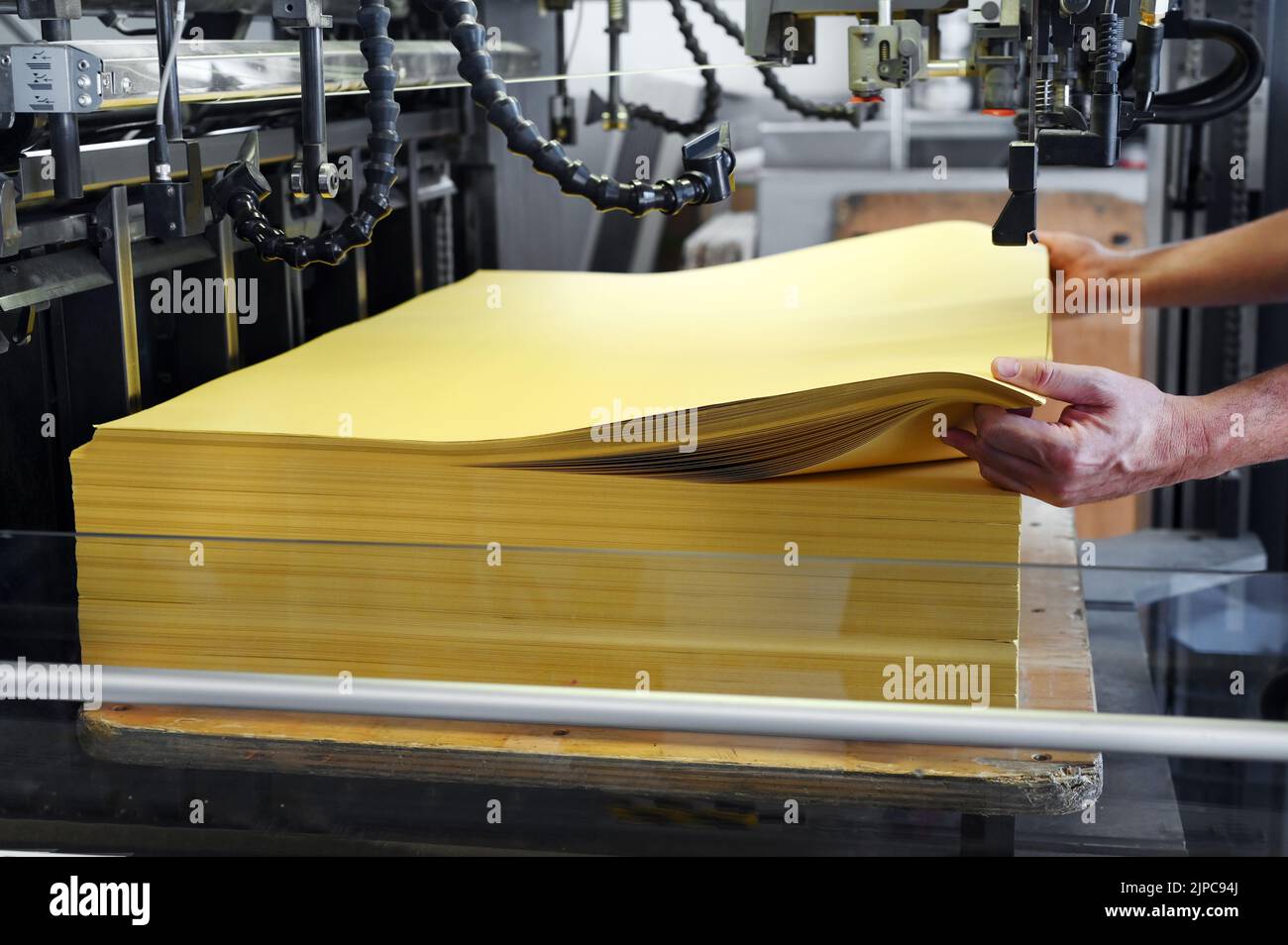 Empleados irreconocibles que ponen hojas de papel amarillo en la máquina de impresión offset durante el trabajo en el taller de tipografía Foto de stock