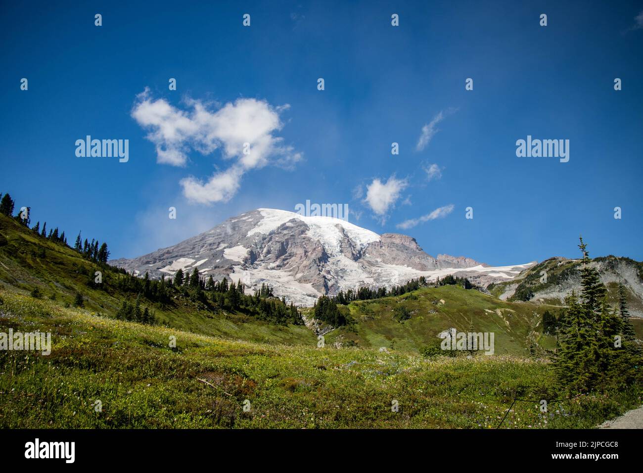 El paisaje de verdes colinas y nevadas en la cima de la montaña bajo el cielo azul Foto de stock