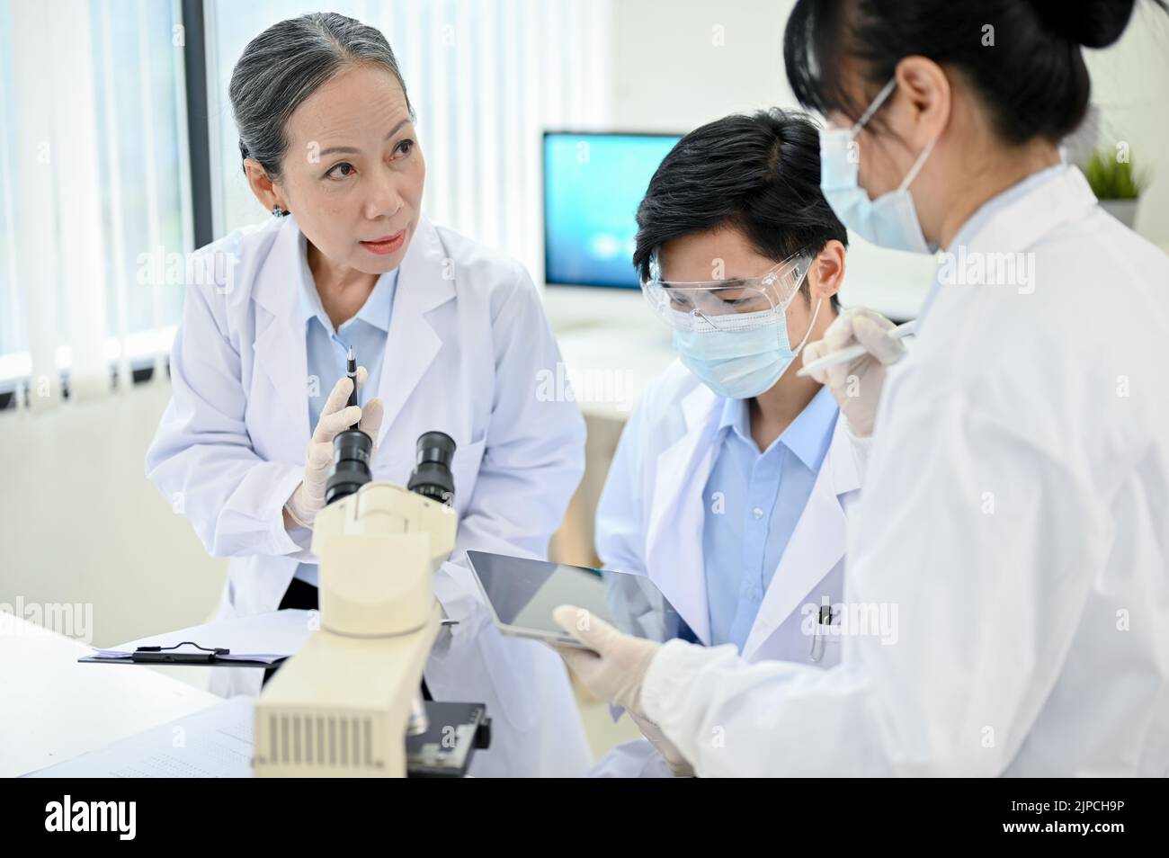 Una supervisora profesional especialista médica superior asiática que capacita en el laboratorio a dos jóvenes especialistas médicos asiáticos menores. Foto de stock