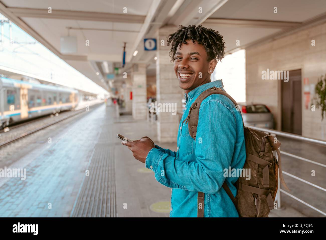 Un hombre sonriente de pie de lado a la cámara cerca del ferrocarril Foto de stock