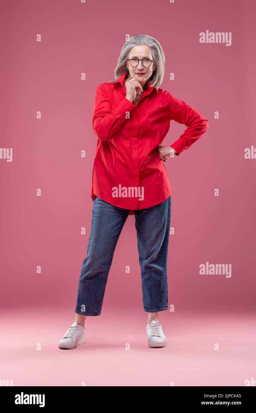 Mujer con camisa roja de pie y tocando la barbilla Foto de stock