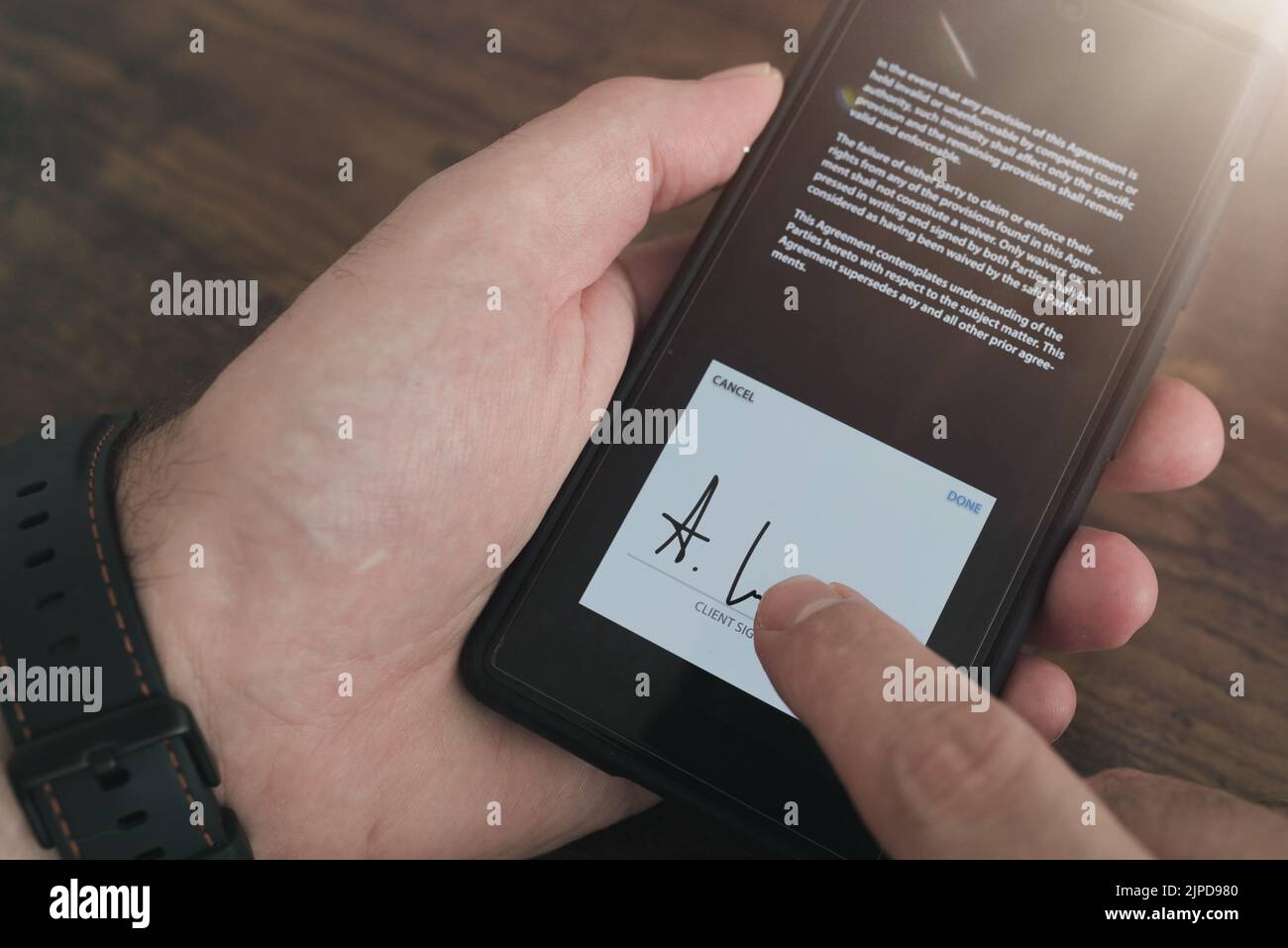 vista de primer plano de la firma electrónica con el dedo en la pantalla táctil del smartphone sobre un fondo de mesa de madera Foto de stock