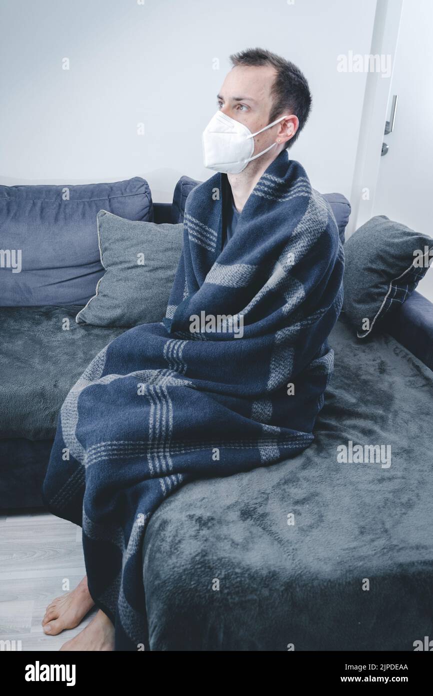 22 Febrero 2021: Hombre con manta sobre sofá en Departamento Frío, Exhaustos, Enfermos y Frío. Migraña y frío en casa en el apartamento con FFP 2 Medical Foto de stock