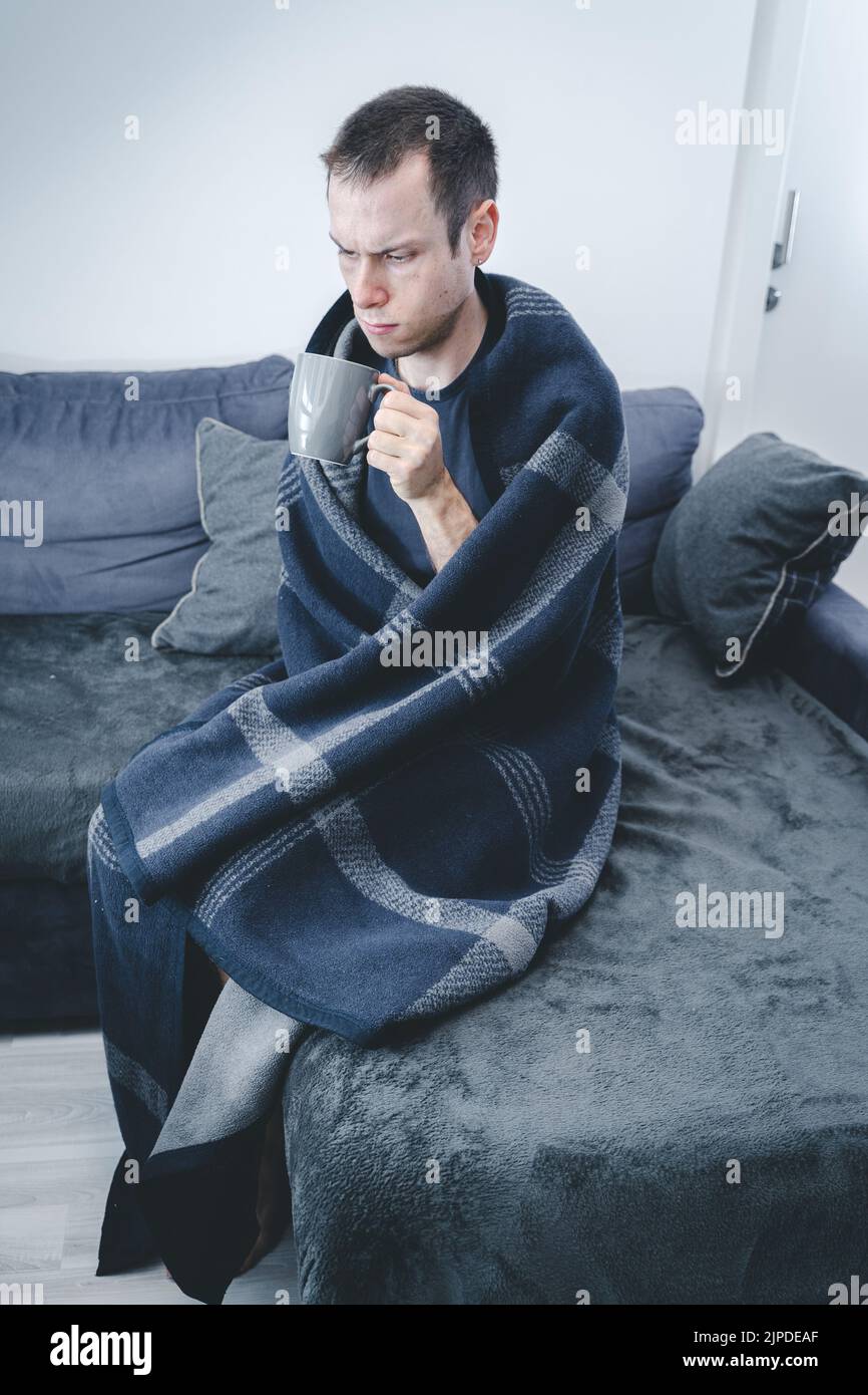 22 de febrero de 2021: Enfermo con gripe sentado en un sofá en casa cubierto con manta caliente. Frío EN APARTAMENTO, ENFERMEDAD, GRIPE, CONCEPTO DE DOLOR Foto de stock