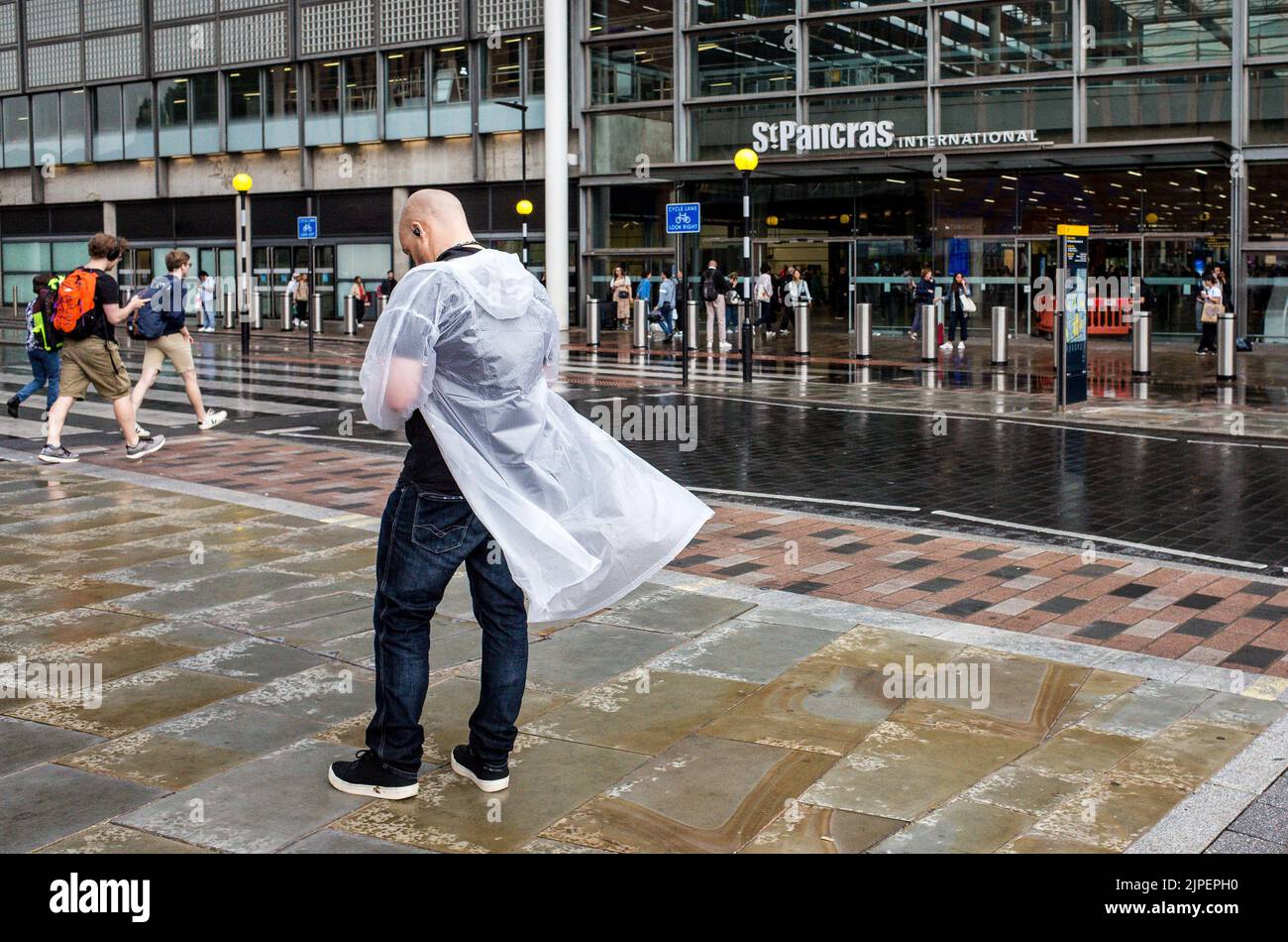 Hombre con impermeable transparente fuera de la estación de tren de St Pancras después de inundaciones repentinas, Londres, verano de 2022, Inglaterra, Reino Unido, El tiempo. Foto de stock