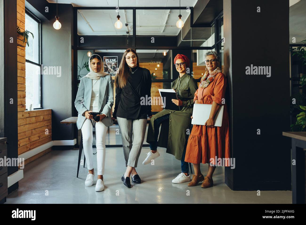 Grupo de diseñadores creativos que miran la cámara en una sala de juntas de la oficina. Empresarias multiculturales que trabajan en equipo en un lugar de trabajo inclusivo. Div Foto de stock