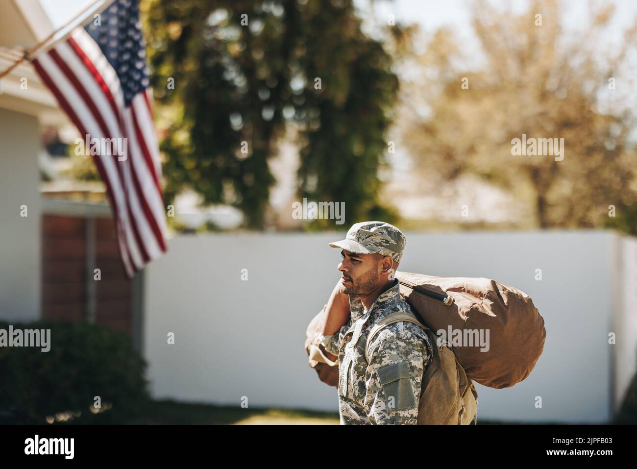 Valiente soldado americano caminando hacia su casa con su equipaje. Joven militar patriótico volviendo a casa después de servir a su país en la milita Foto de stock