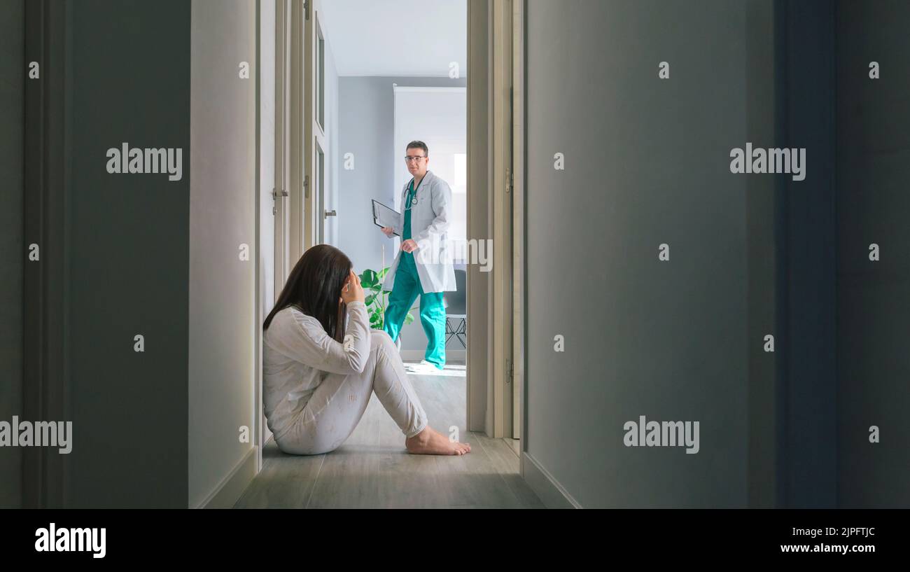 Doctor mirando a una paciente con trastorno mental sentada en el piso del hospital Foto de stock