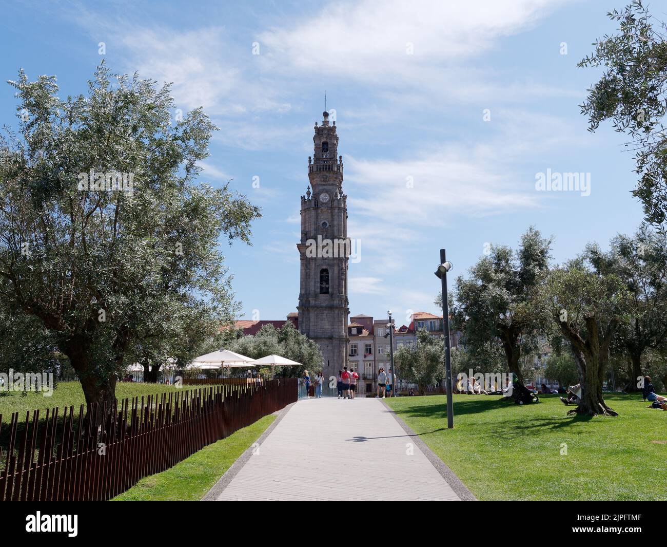 Iglesia de Clérigos, una iglesia barroca en la ciudad de Oporto, Portugal. En el primer plano los turistas caminan y se sientan en una zona de parque llena de olivos. Foto de stock