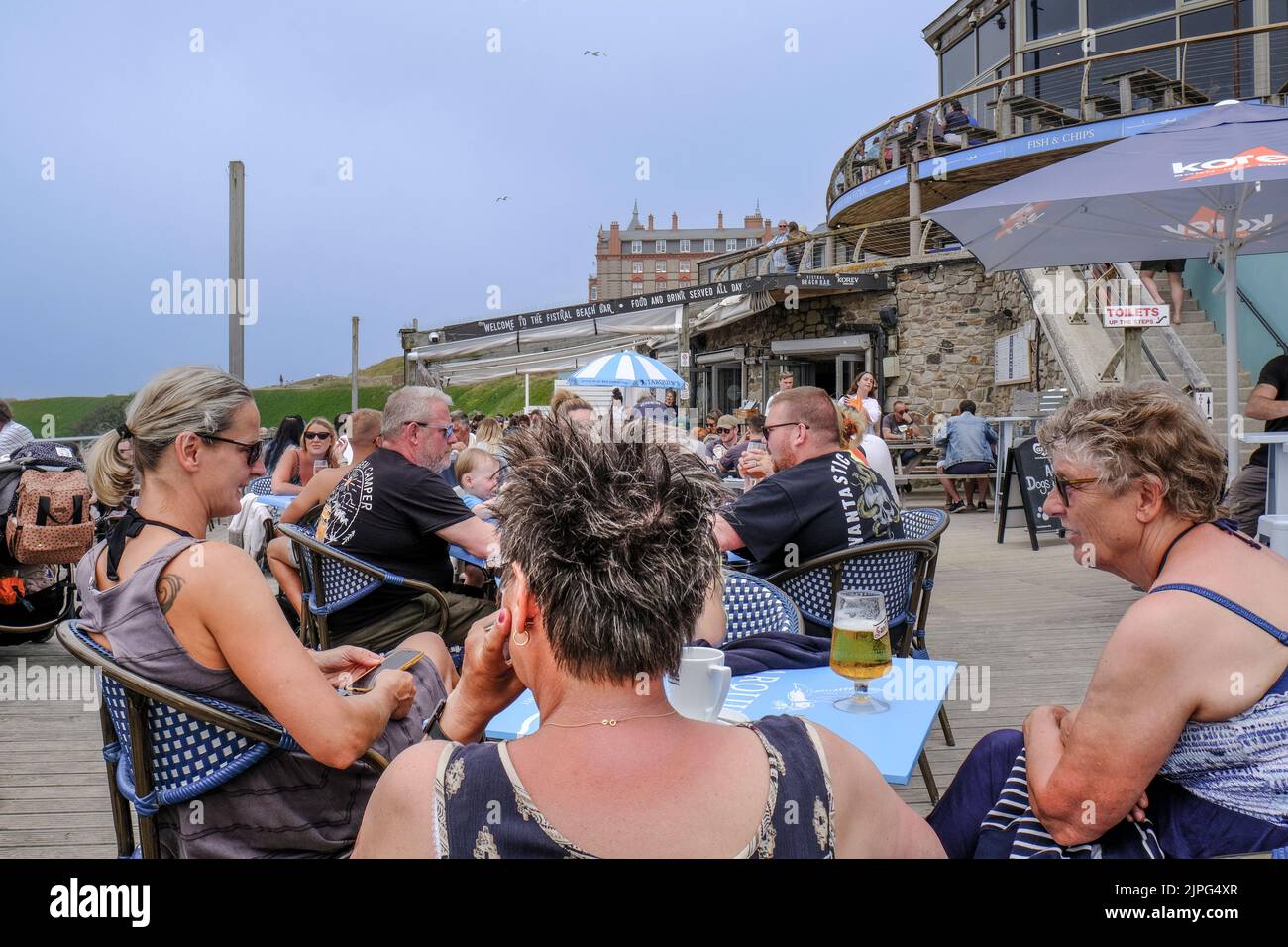 En uno de los días más calurosos del año, los turistas del Reino Unido se relajan en la zona de terrazas del Fistral Beach Bar en Newquay, en la costa de Cornwall. Foto de stock