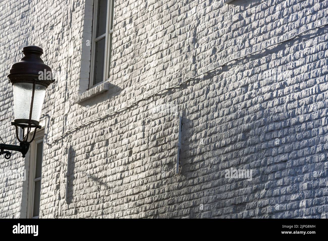 Lámpara de calle en el fondo de una pared de ladrillo pintado de color blanco bajo una luz de rastrillo. Foto de stock