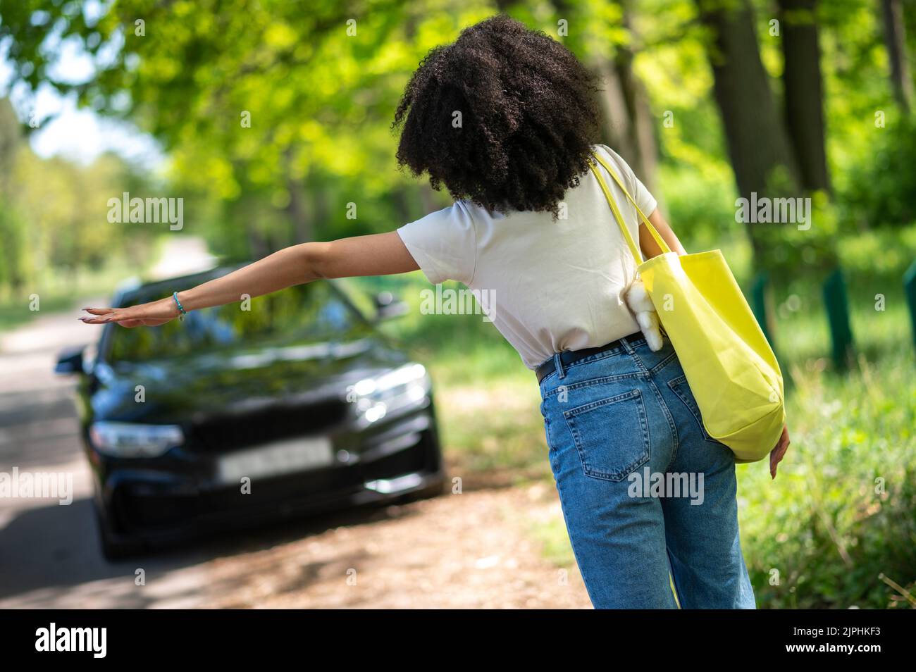 Chica joven con pelo rizado autostop y luciendo emocionado Foto de stock