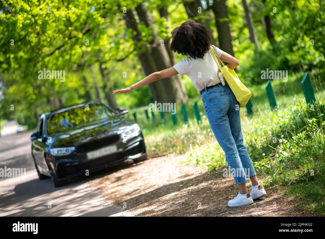 Chica joven con pelo rizado autostop y luciendo emocionado Foto de stock