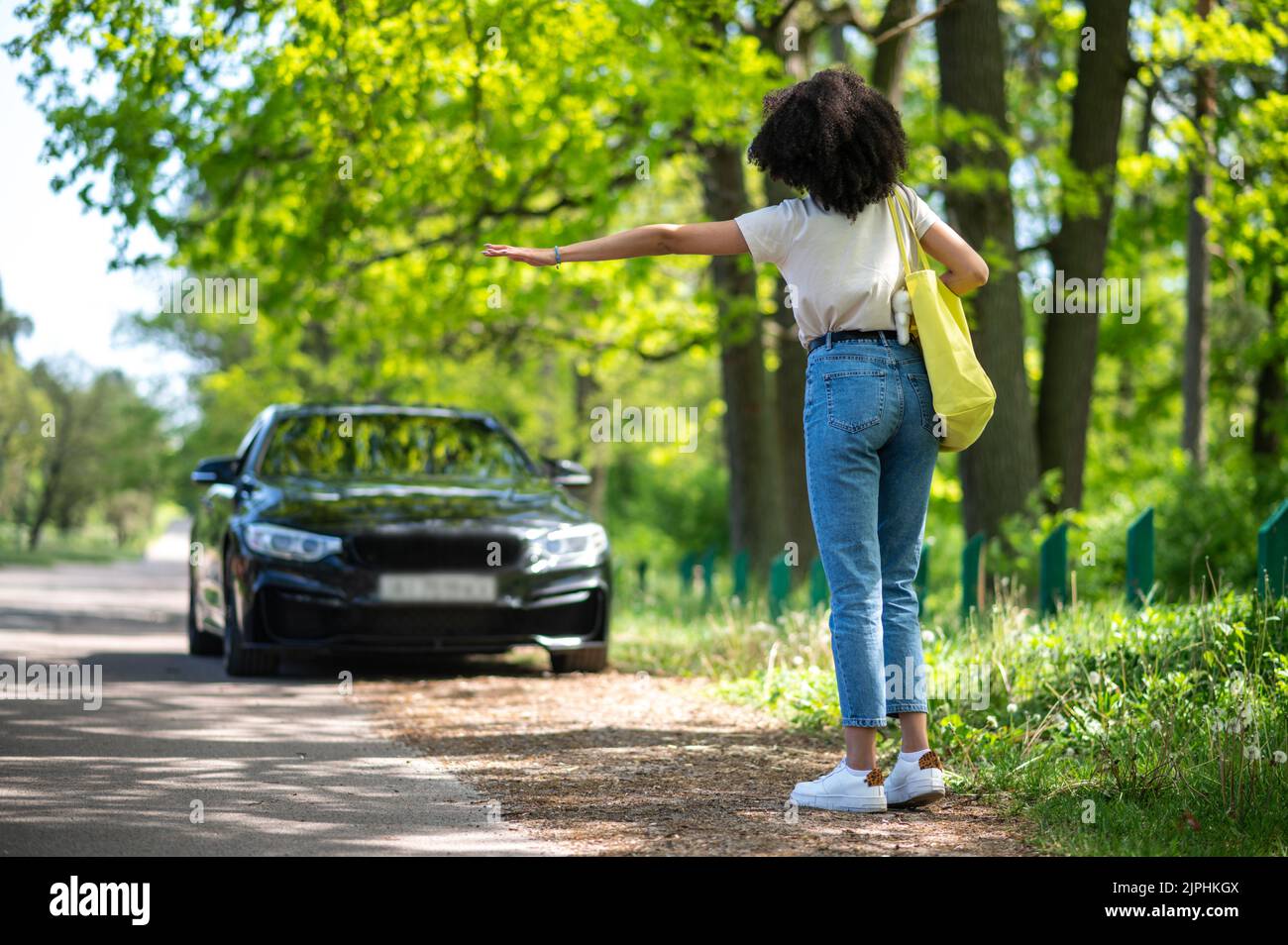 Mujer joven y delgada de pelo rizado que detiene el coche en el parque Foto de stock
