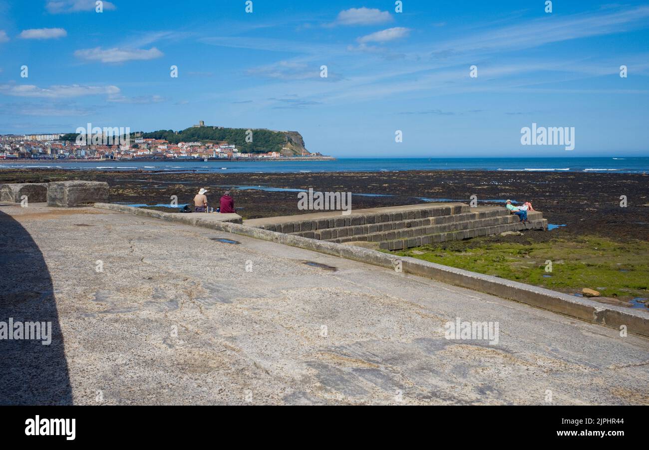 Parejas mayores sentadas en el mar con el castillo de Scarborough y el casco antiguo en el fondo Foto de stock