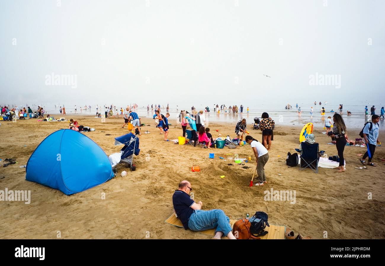 Escena animada en la playa de Scarborough durante un fin de semana de verano, con muchas familias asiáticas en el agua y en la arena Foto de stock