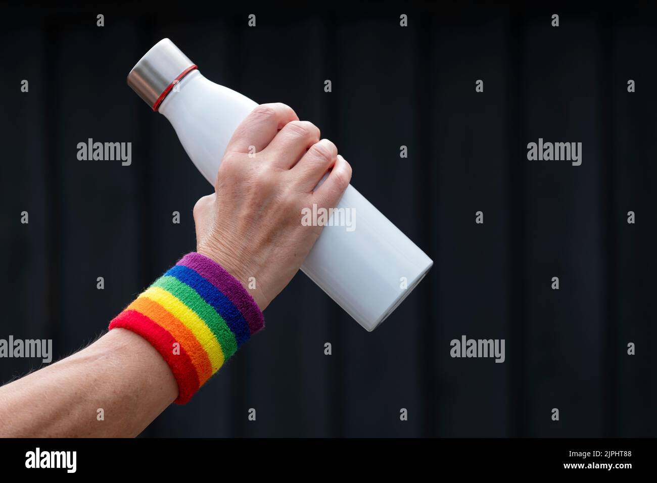 Una mujer de mediana edad que llevaba una banda de sudor Gay Pride alrededor de su muñeca. Ella sostiene una botella de bebidas para que pueda rehidratarse mientras está entrenando. Foto de stock