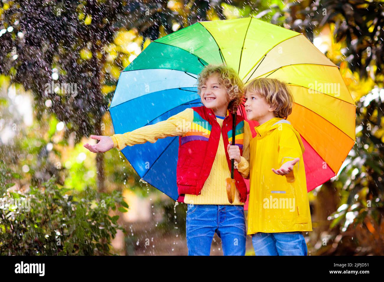Niños jugando bajo la lluvia de otoño. Niño con paraguas. Niño corriendo en  la calle de la ciudad en la temporada de otoño. Diversión al aire libre  para los niños en cualquier