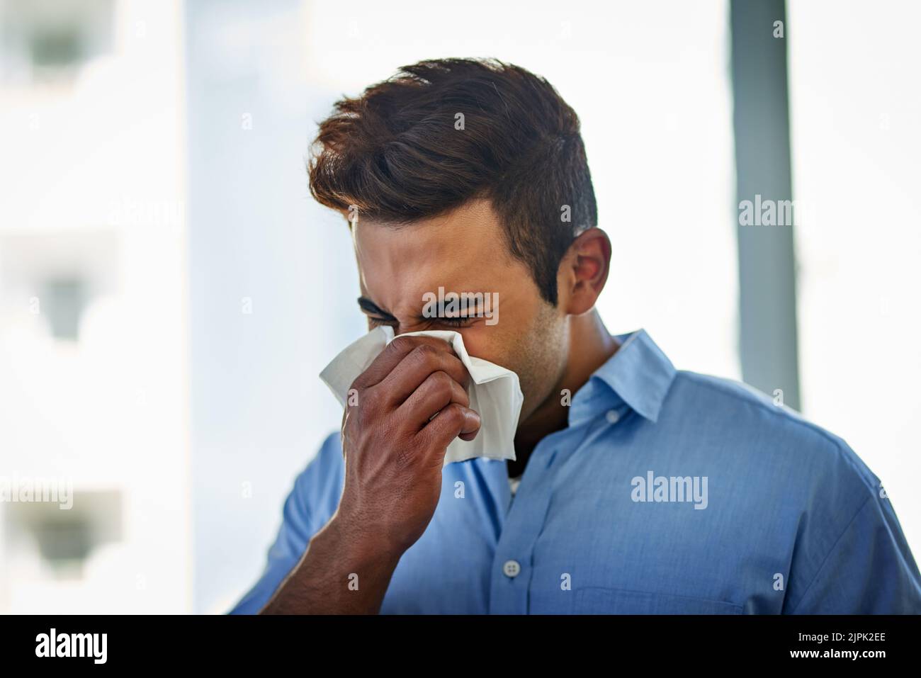 Necesita un refuerzo inmunológico para su defensa contra la gripe, un joven hombre de negocios que se sopla la nariz en el trabajo. Foto de stock