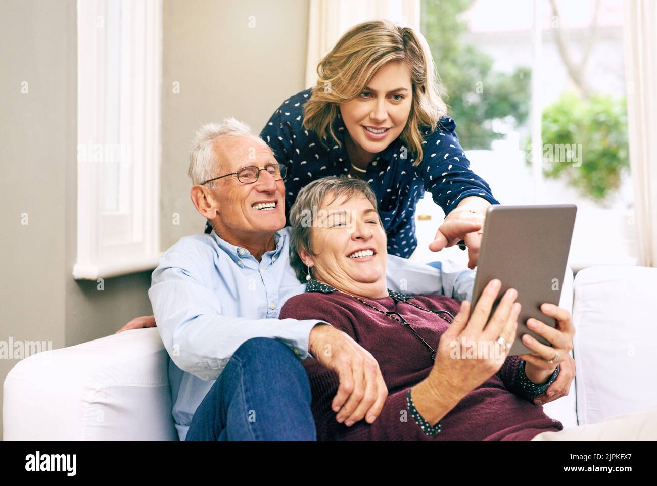 ¿Qué piensa de esta aplicación que he descargado. Una hija adulta y sus padres mayores usando una tableta juntos en casa. Foto de stock