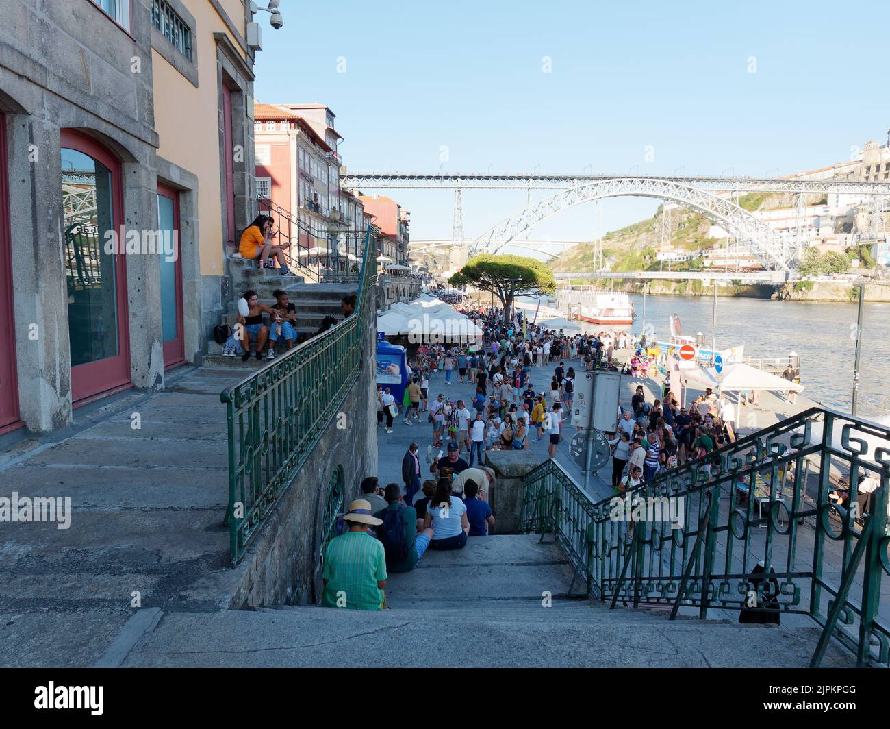 Gente relajándose en las escaleras del distrito Ribeira, también conocido como distrito ribereño de Porto, Portugal, con el río Duoro a la derecha y el puente Luis I detrás. Foto de stock