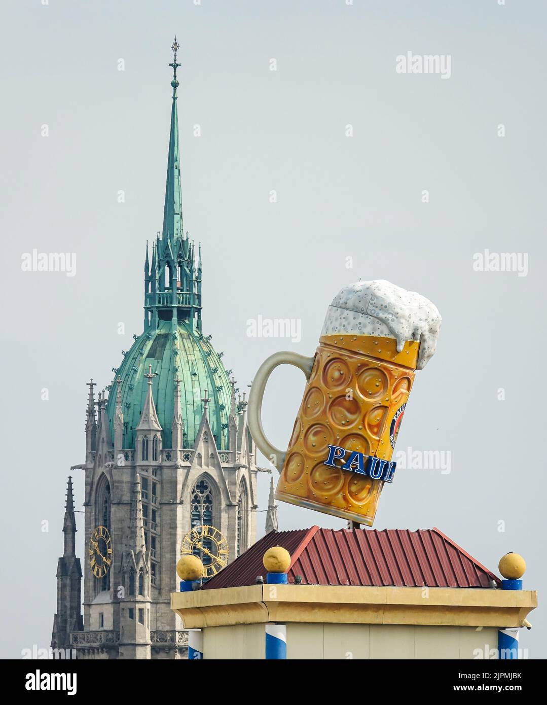 Oktoberfest de Múnich, una gran taza de cerveza en Theresienwiese con el telón de fondo de la iglesia gótica de San Pablo. Munich, ALEMANIA - Agosto de 2022 Foto de stock