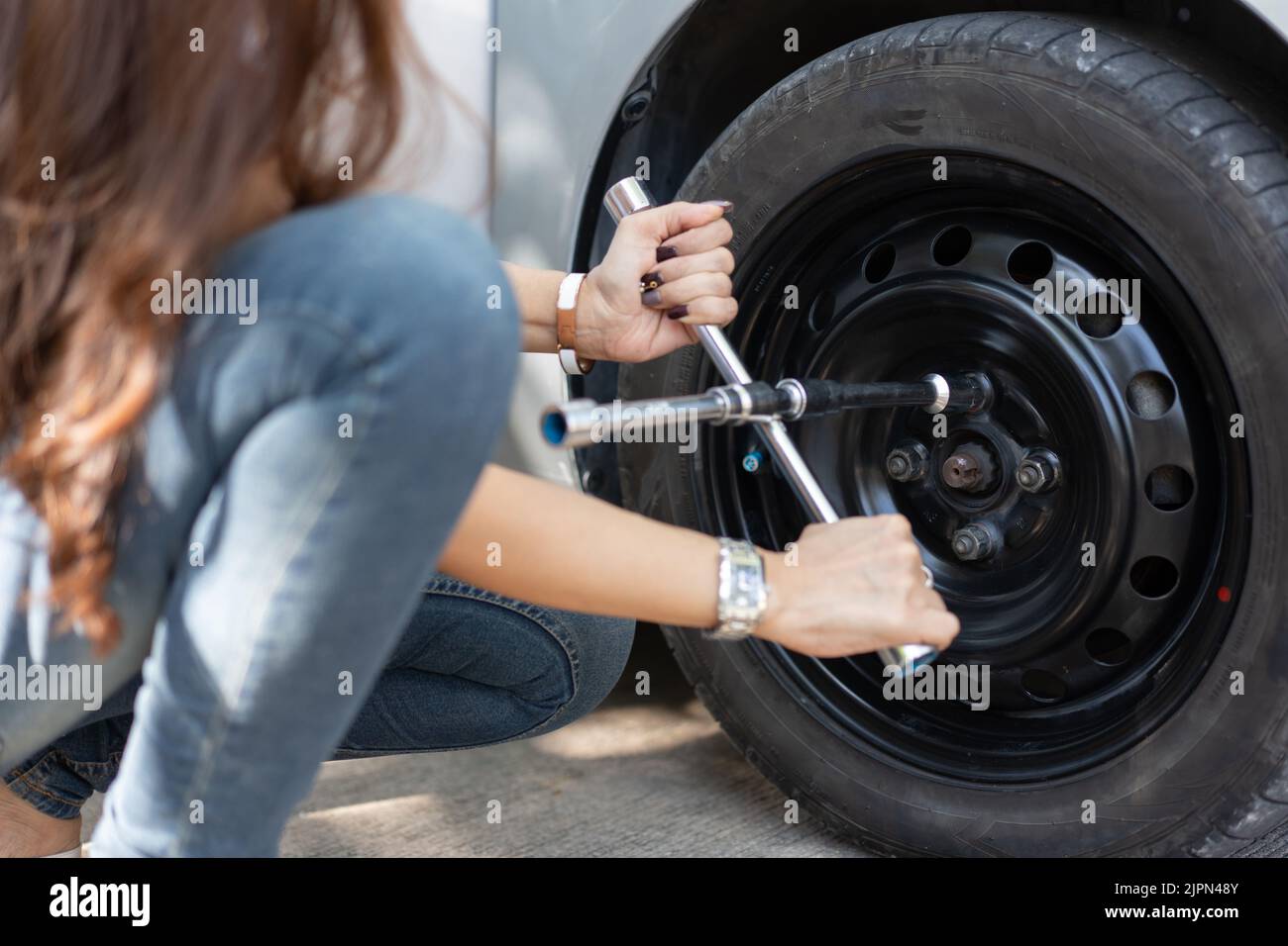 Mujer joven con la llave para cambio de ruedas en un coche roto Fotografía  de stock - Alamy