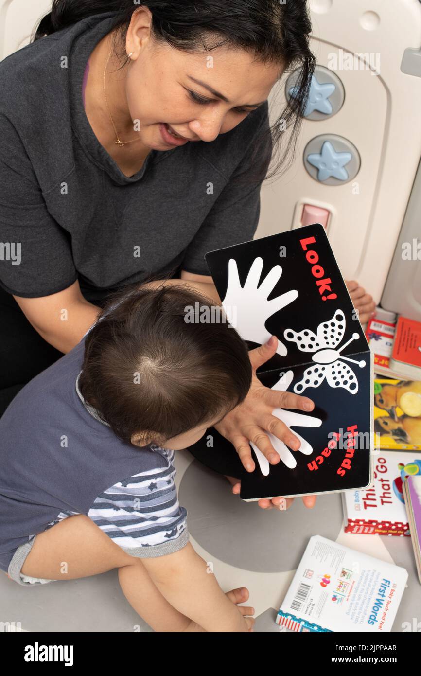 niño de 11 meses de edad en casa con la madre, leer a, interesado como ella muestra su mano sobre una ilustración de una mano Foto de stock