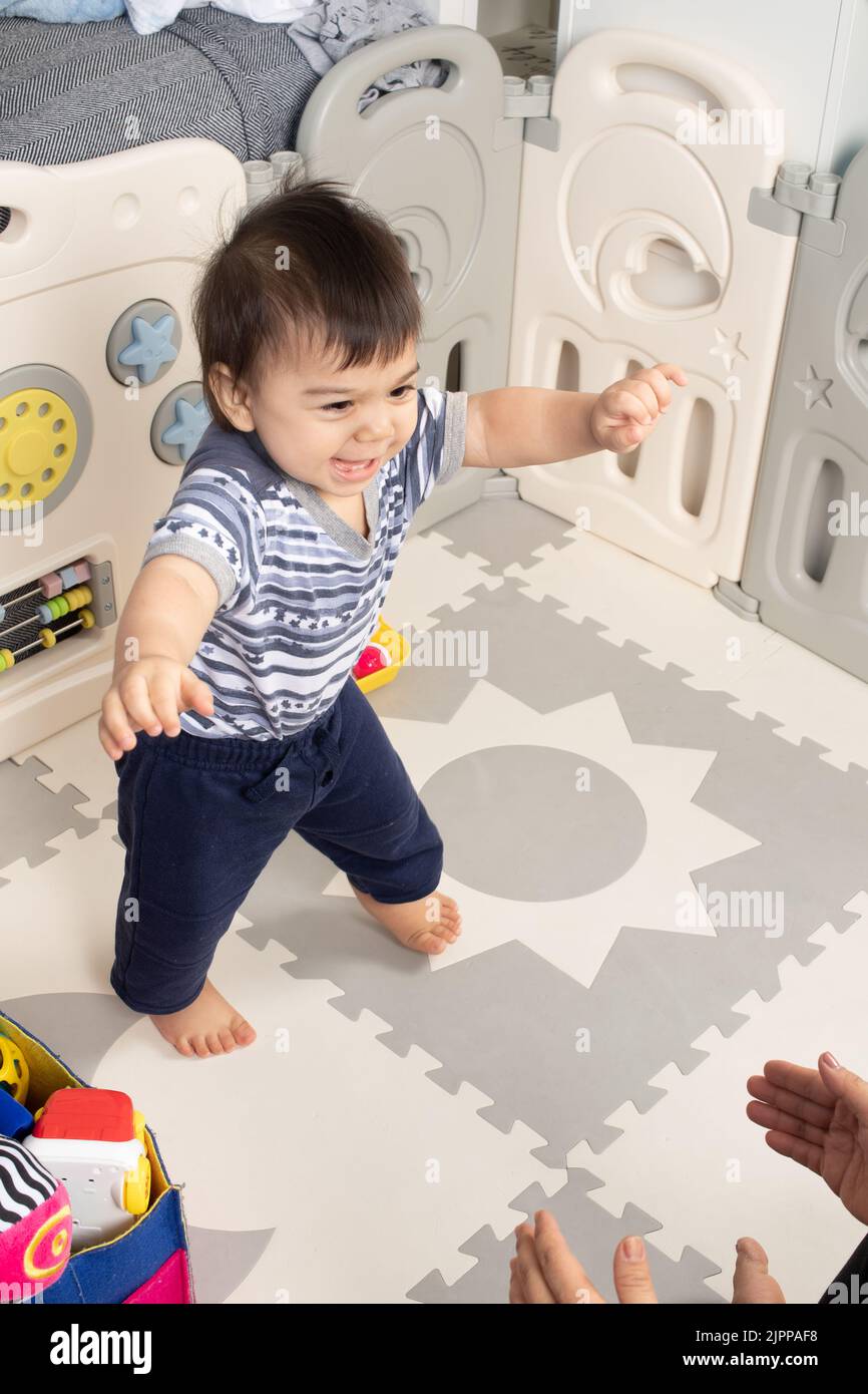 niño de 11 meses caminando hacia las manos abiertas de la madre primeros pasos feliz Foto de stock