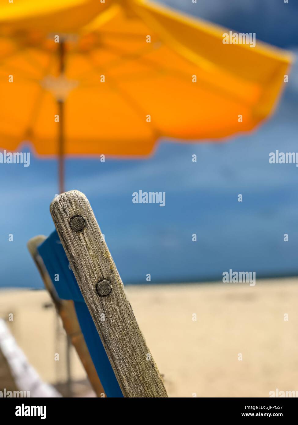 Un primer plano de una silla de madera y una sombrilla amarilla de playa transmiten una tranquila escena de playa del sur de Florida. Foto de stock