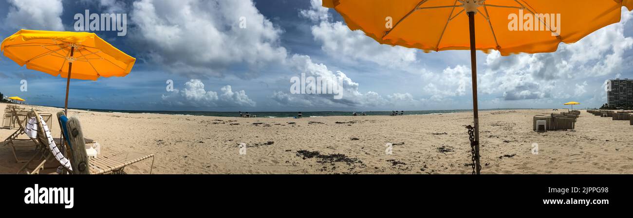 Panorama muestra sombrillas amarillas, cielo azul cobalto y playa de arena a lo largo de la costa de Fort Lauderdale. Foto de stock