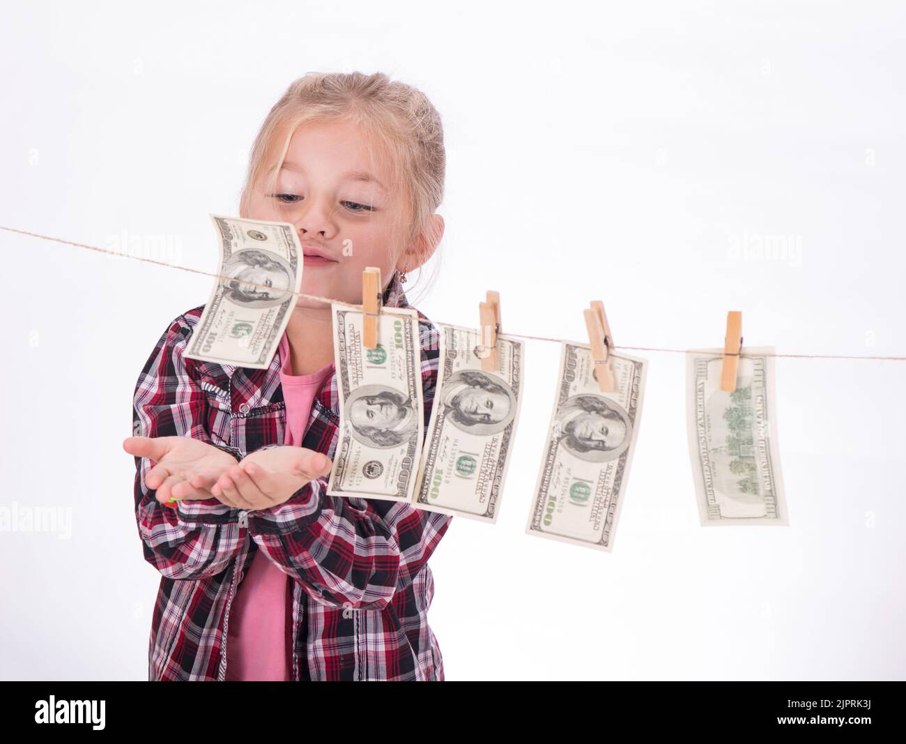 los niños y el dinero. Chica colgando billetes de dólar en una cuerda aislada sobre fondo blanco Foto de stock