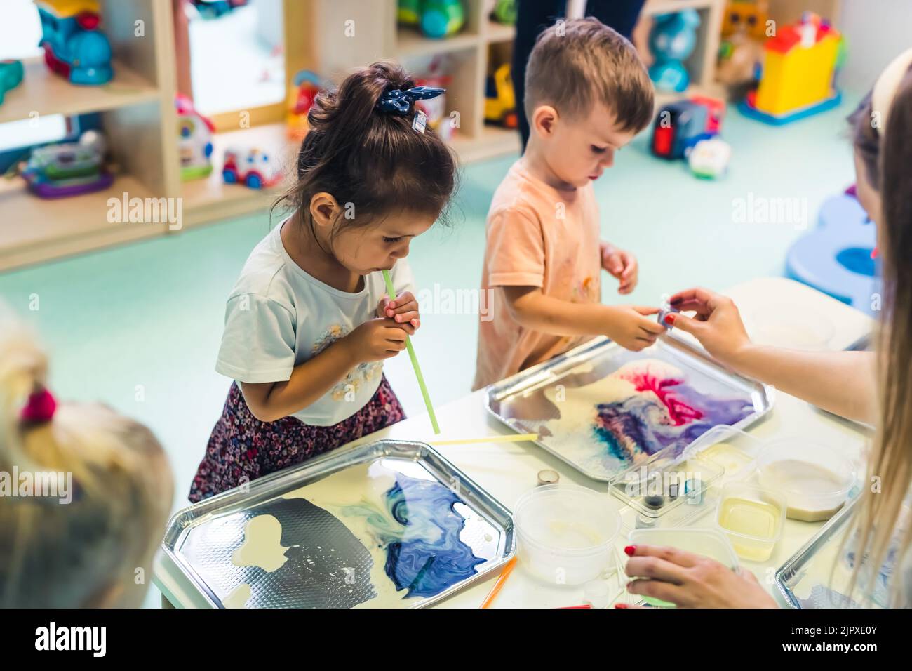 Guardería multicultural. Niños pequeños jugando con pajuelas rayadas y pintando con leche, usando colorantes alimenticios no tóxicos para los colores. Actividades creativas para los niños para usar sus sentidos y el desarrollo cerebral. Habilidades motoras finas. Fotografía de alta calidad Foto de stock