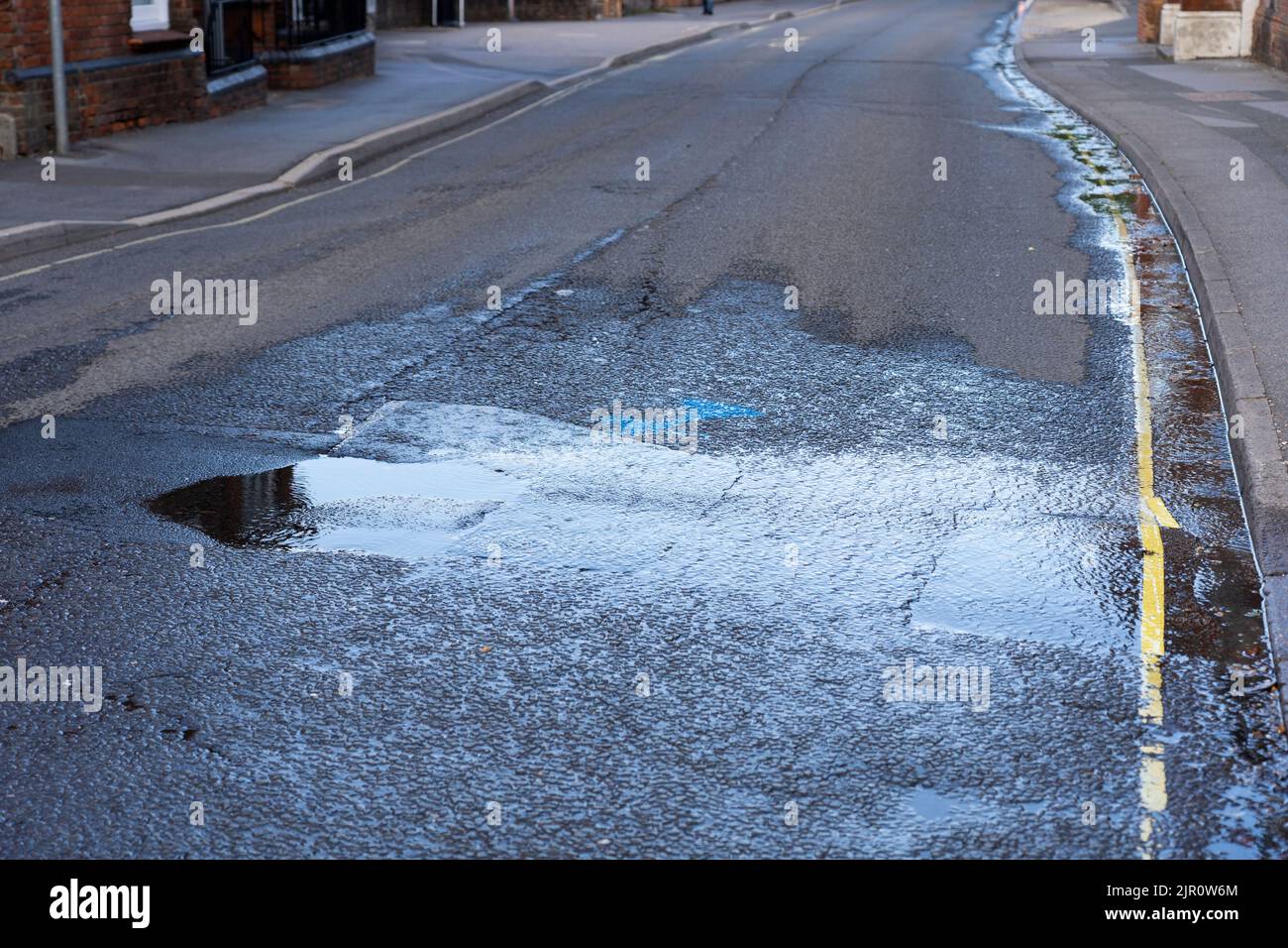 Al final de la sequía de 2022, una tubería de agua en la carretera de Winchester hace que el agua se derrame por la carretera y se pierda por el desagüe. Basingstoke. REINO UNIDO Foto de stock