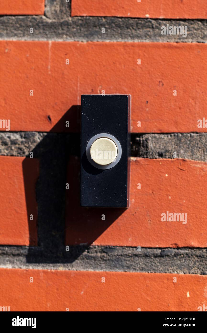 Un retrato de cerca de un viejo timbre negro con un botón blanco en una pared de ladrillo rojo, listo para ser presionado para tocar el timbre y notificar a los residentes. Foto de stock